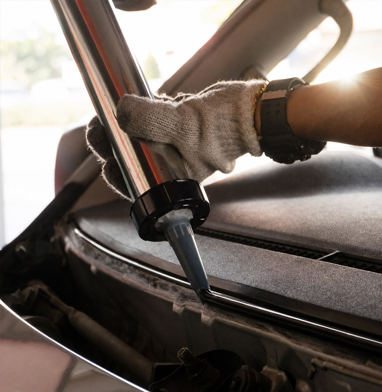 perfect-adhesive-bead-on-windshield-replacement - American Auto Glass Solutions Close-up of a technician's gloved hand guiding a windshield into place with a suction-type installation tool on a car.